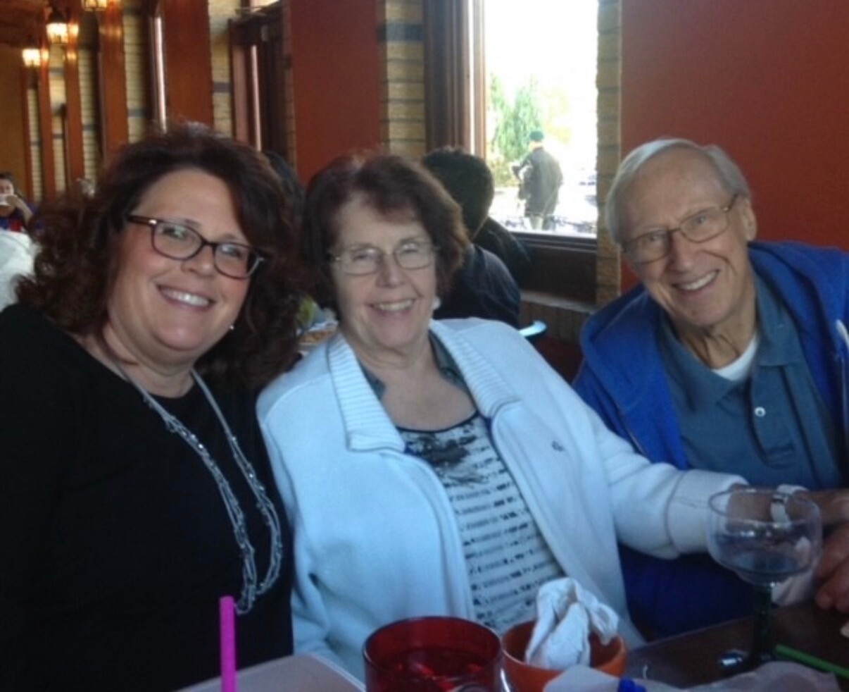 Three friends sit smiling at a restaurant table, with drinks in front of them.