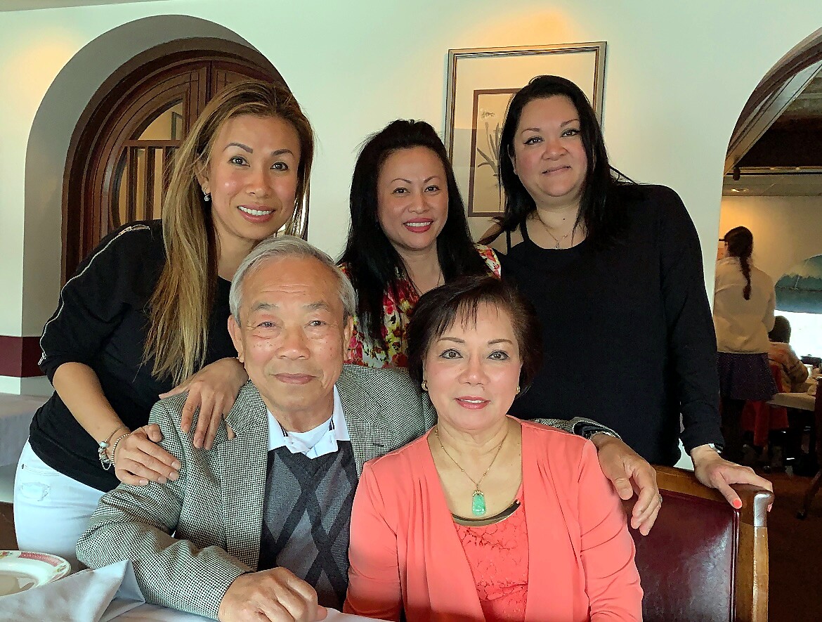 Five adults posing for a group photo at a restaurant, two seated in front and three standing behind them, all smiling.