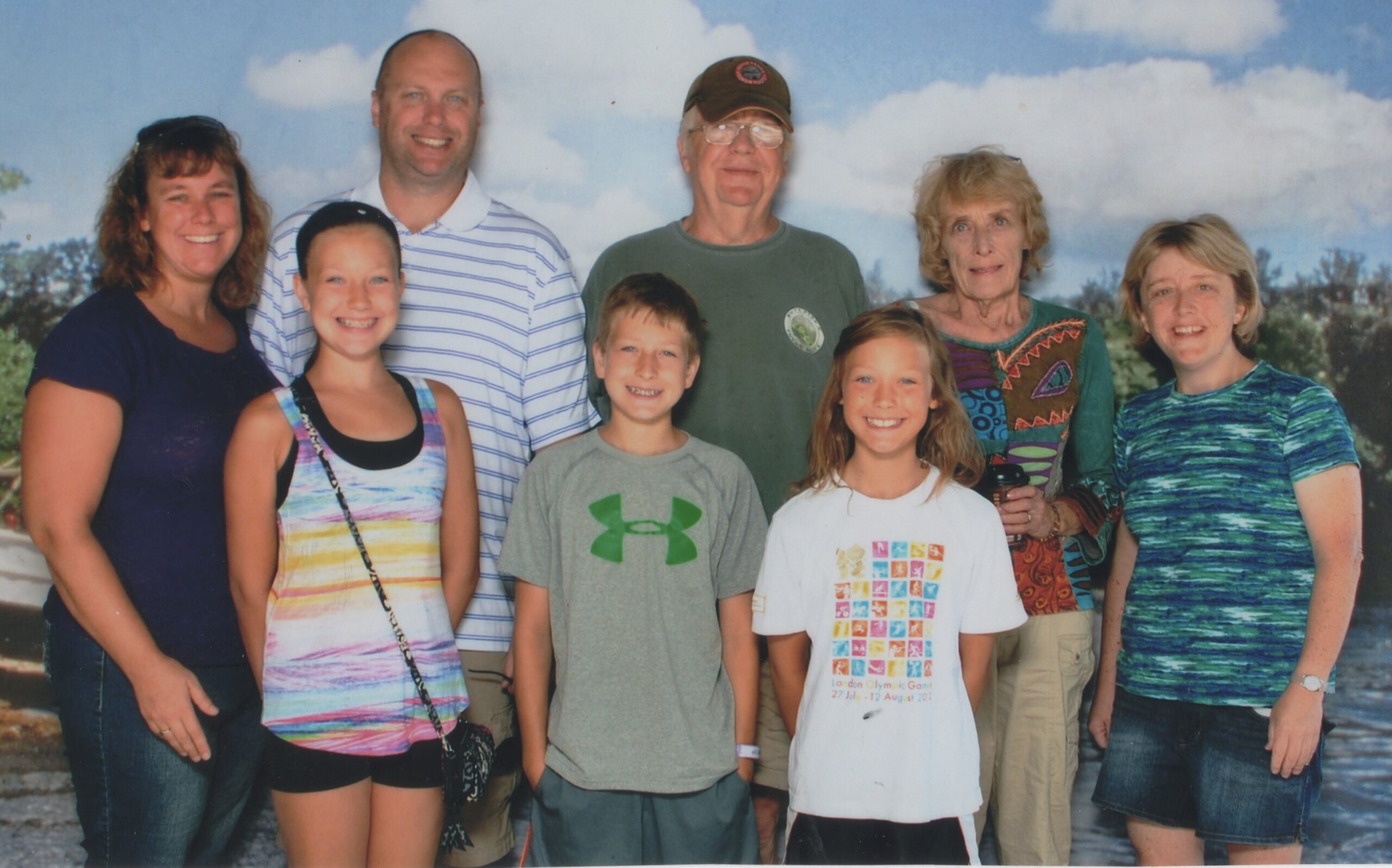 Eight family members posing outdoors, smiling in front of a blue sky backdrop.