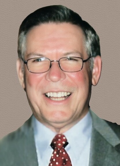 Smiling middle-aged man wearing glasses, light blue shirt, red polka dot tie, gray suit, against a beige textured background.