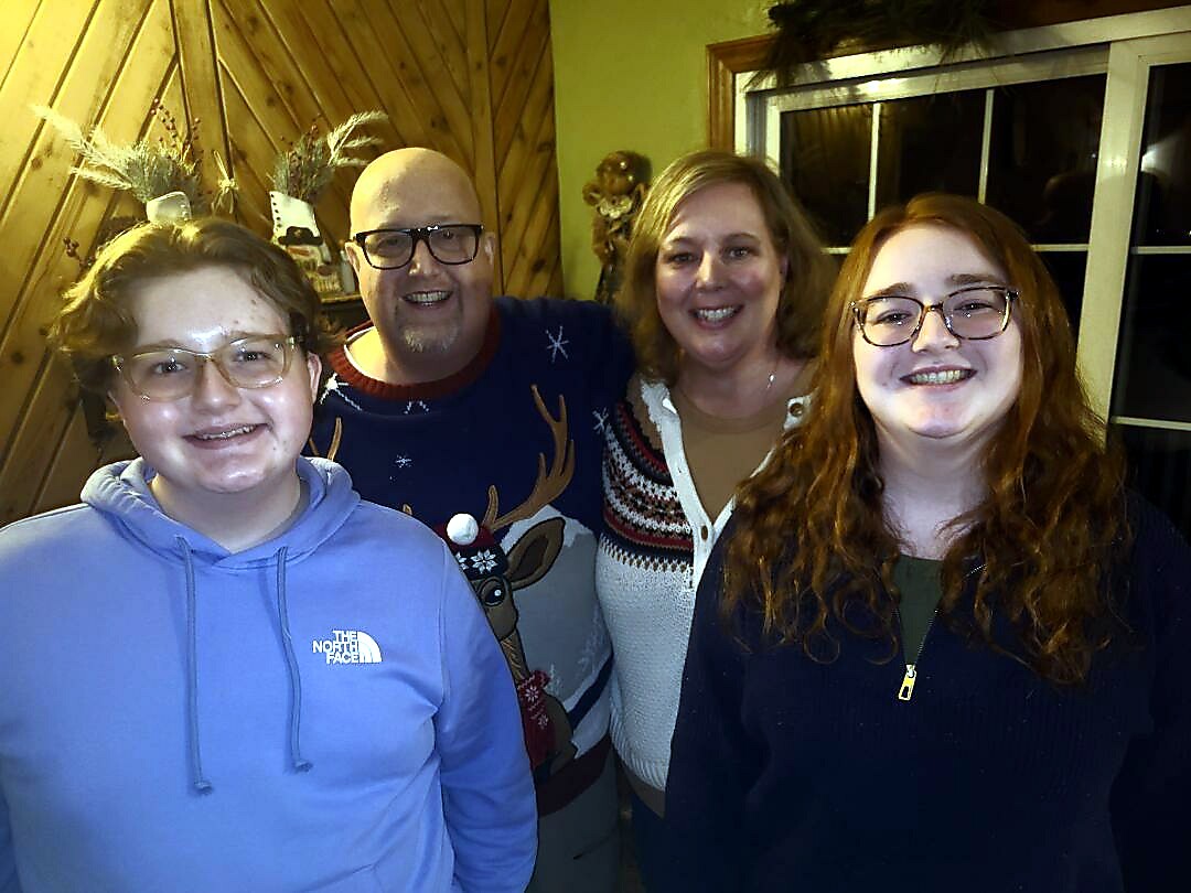 Four people posing in a wood-paneled room, all smiling at the camera.