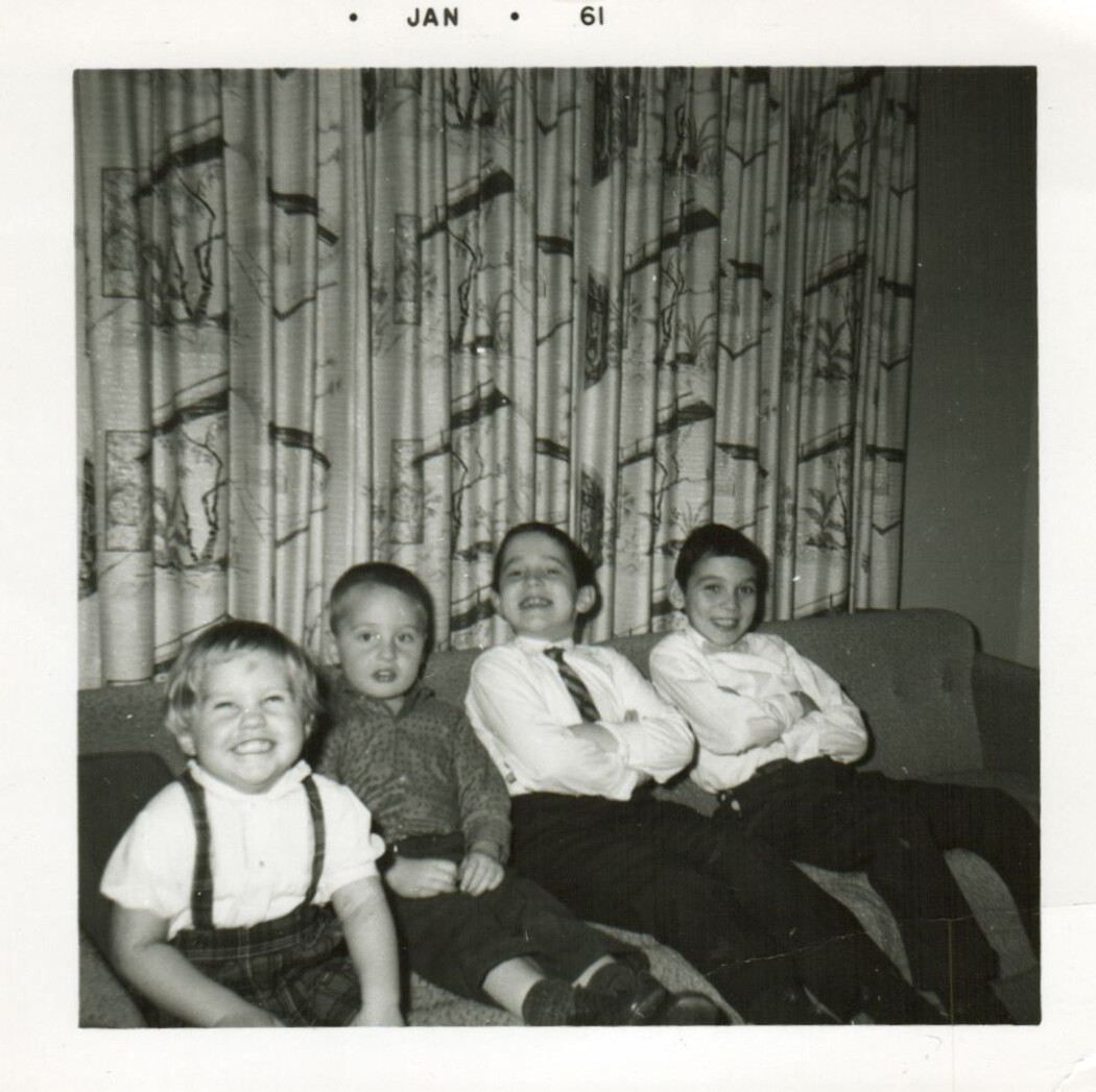 Four children sit on a couch in a living room, smiling; patterned curtains behind them, January 1961 stamp.
