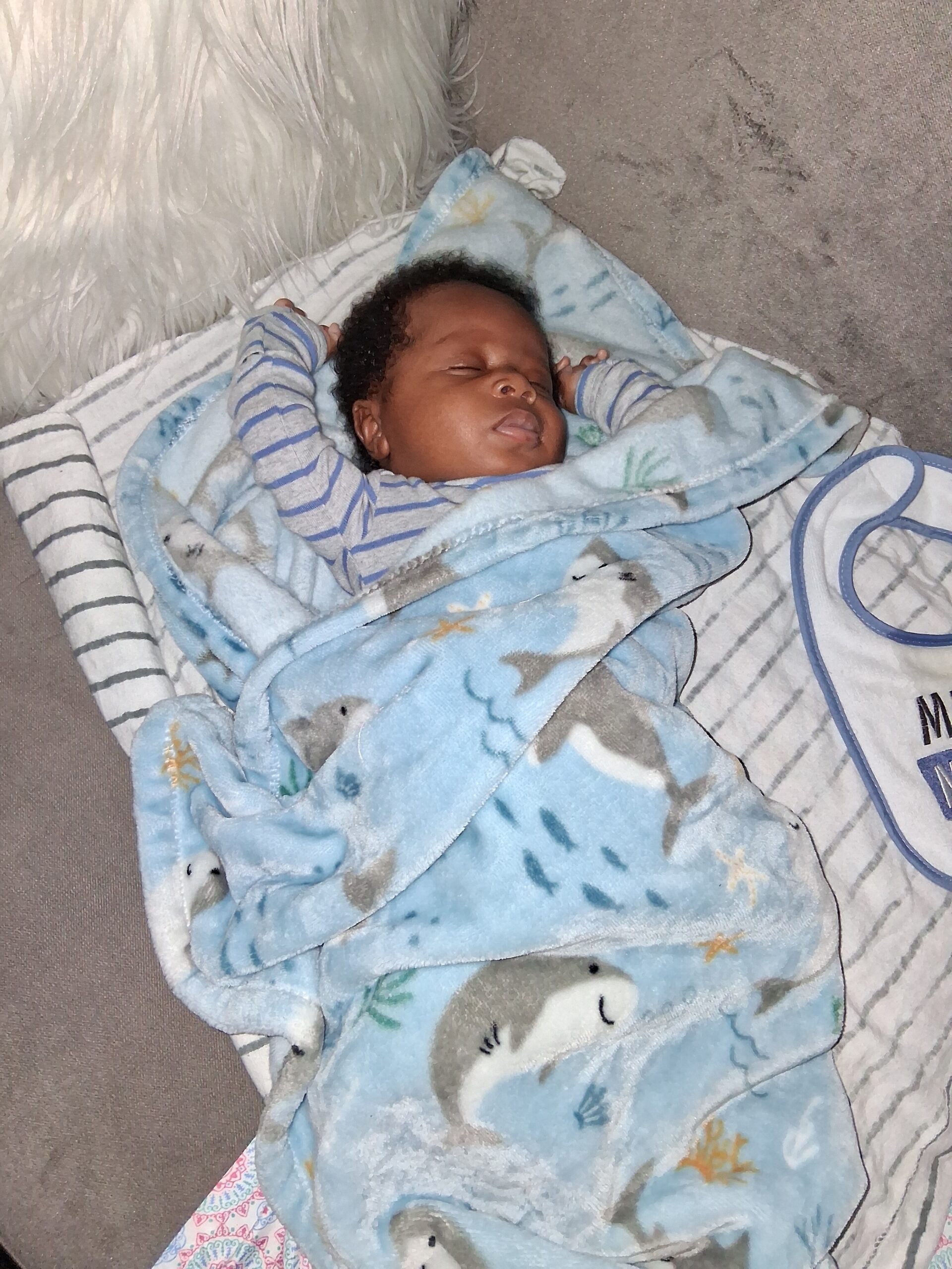 Newborn baby asleep, wrapped in a blue blanket on a striped blanket.