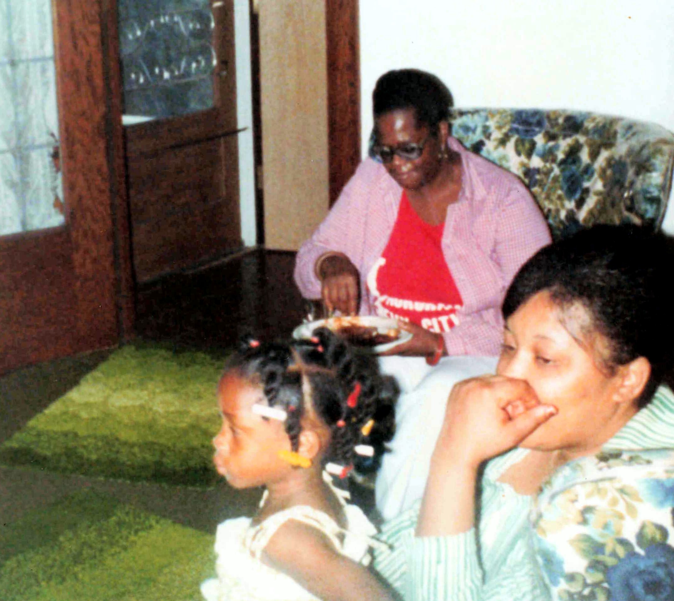 Woman wearing pink shirt and sunglasses sitting on a floral couch in a living room, with children nearby.