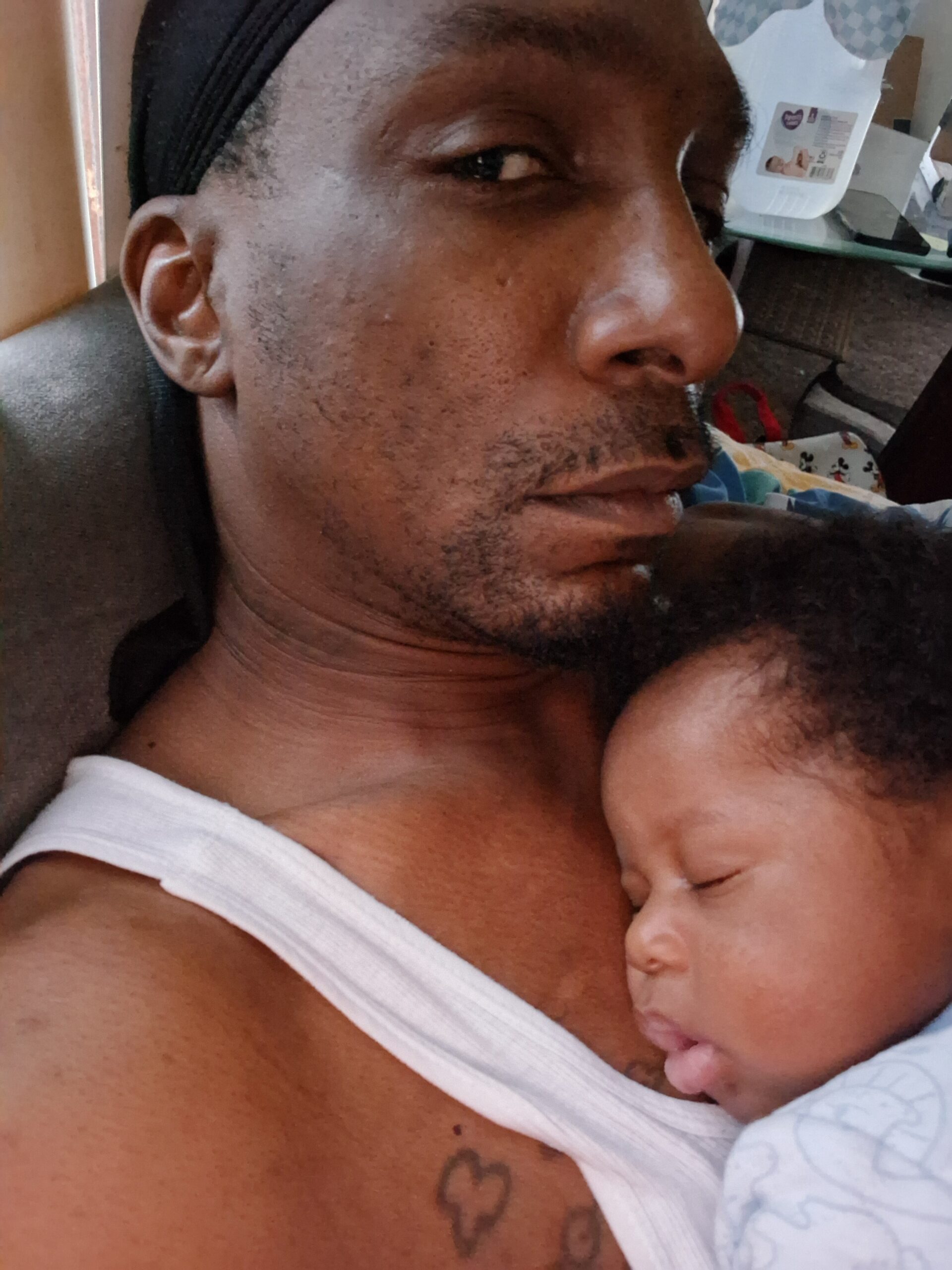 Man lying back with a sleeping baby resting on his chest, both shown in a close-up.
