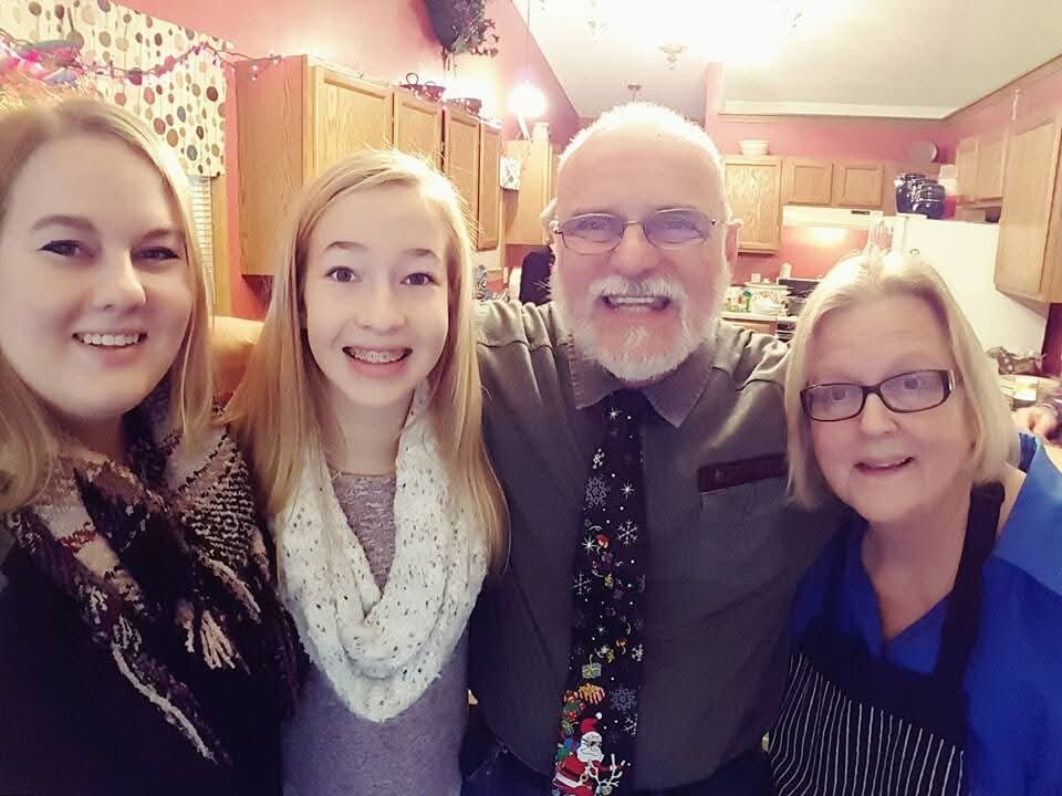 Four adults pose for a group photo in a home kitchen, all smiling at the camera.