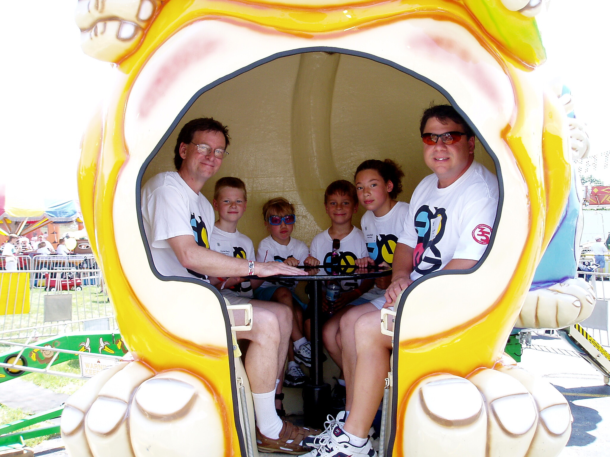 People seated inside a large yellow mouth-shaped amusement ride capsule at a fairground attraction.