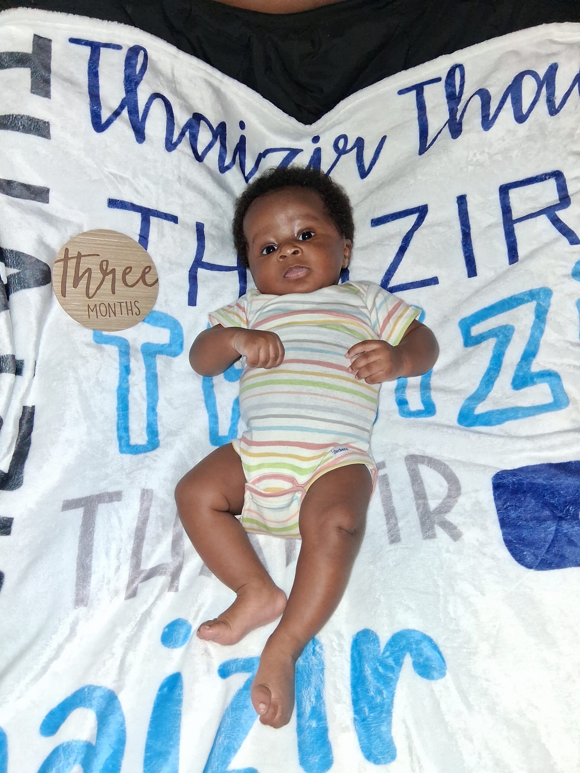 Baby lying on a white blanket with blue letters and a circular 