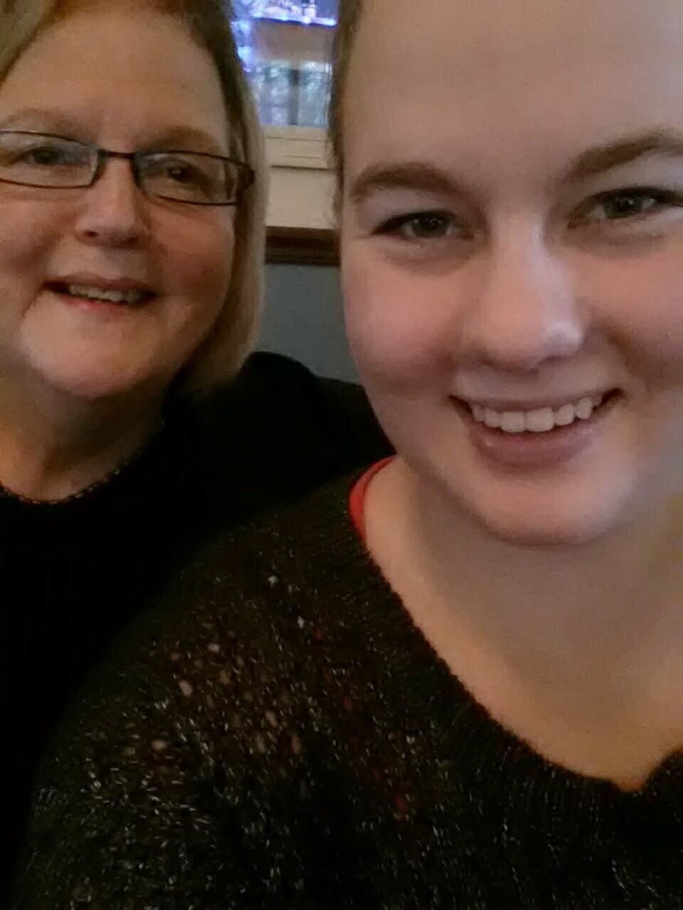Two smiling women posing for a close-up selfie, one wearing glasses on the left and the other on the right indoors.
