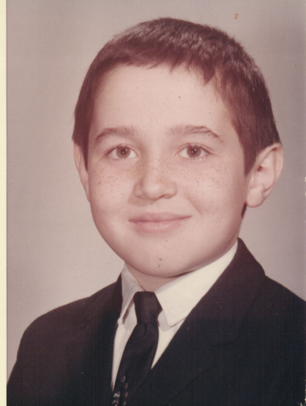 Young boy with short dark hair in a suit and tie, smiling for a formal portrait.