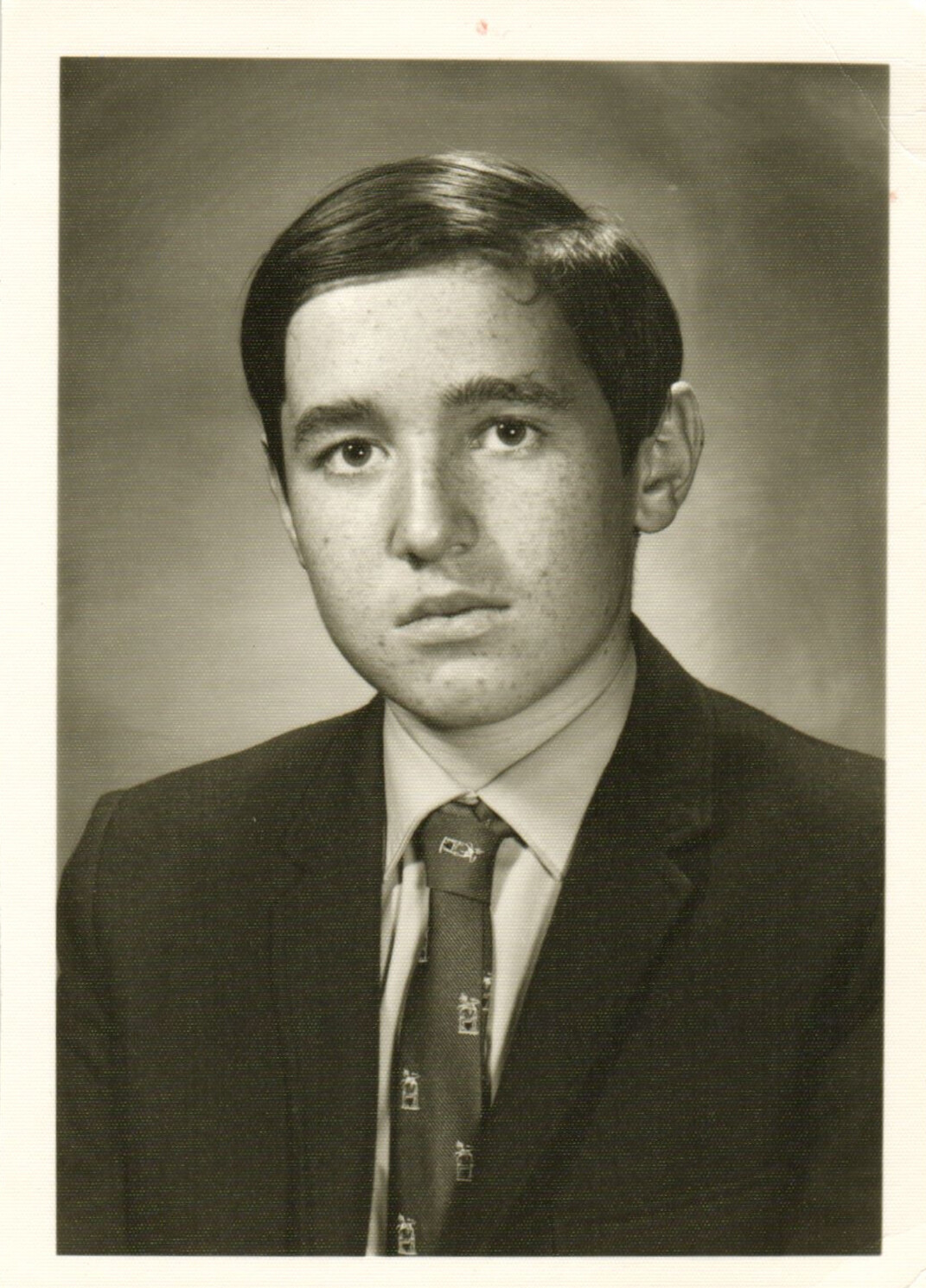 Young man in a dark suit and patterned tie posing for a formal studio portrait.