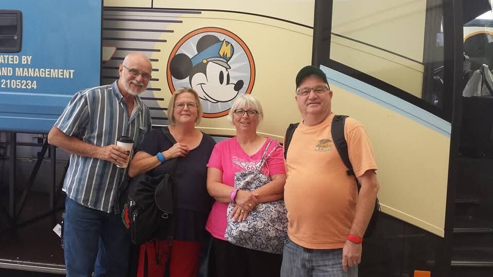 Four adults posing in front of a tour bus with a Mickey Mouse logo on the side.