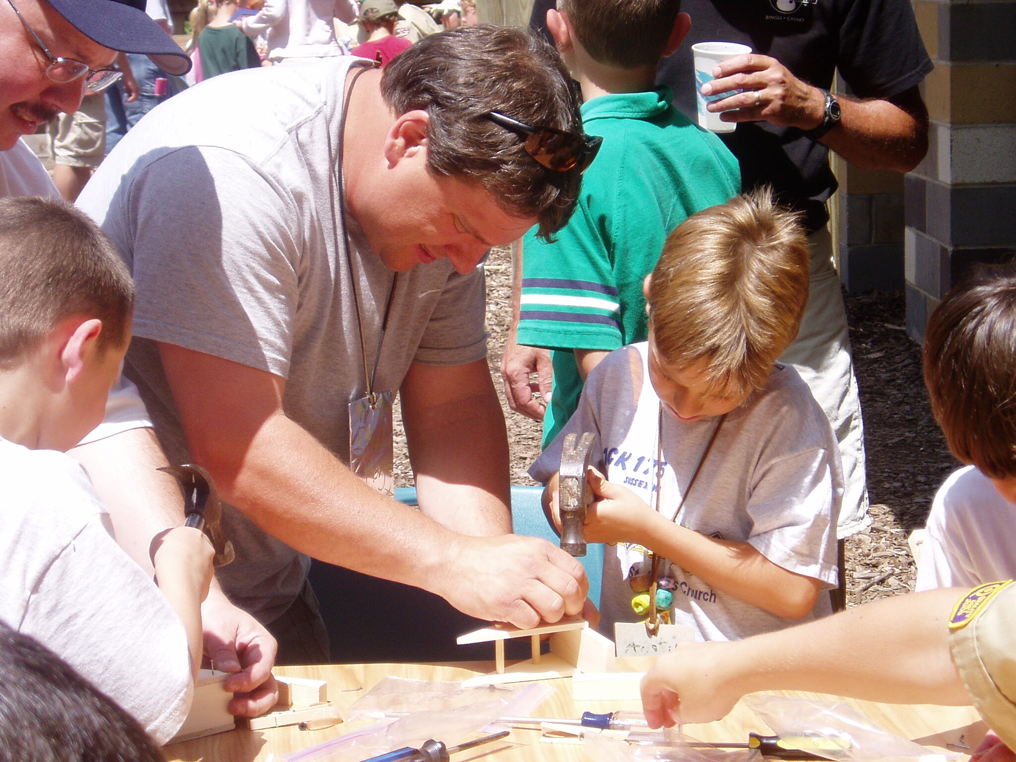 Group of children and adults building wooden blocks on a table outdoors.