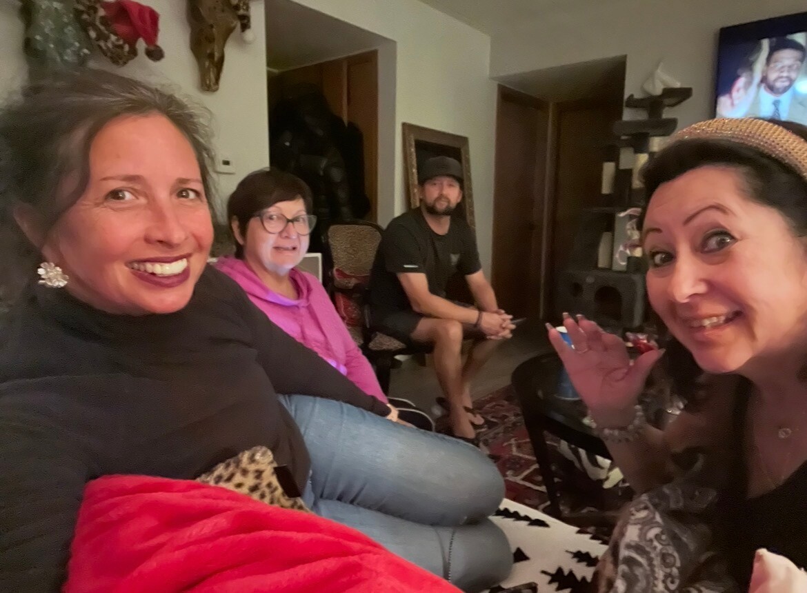 Four adults in a living room posing for a selfie; woman on the right waves at the camera.