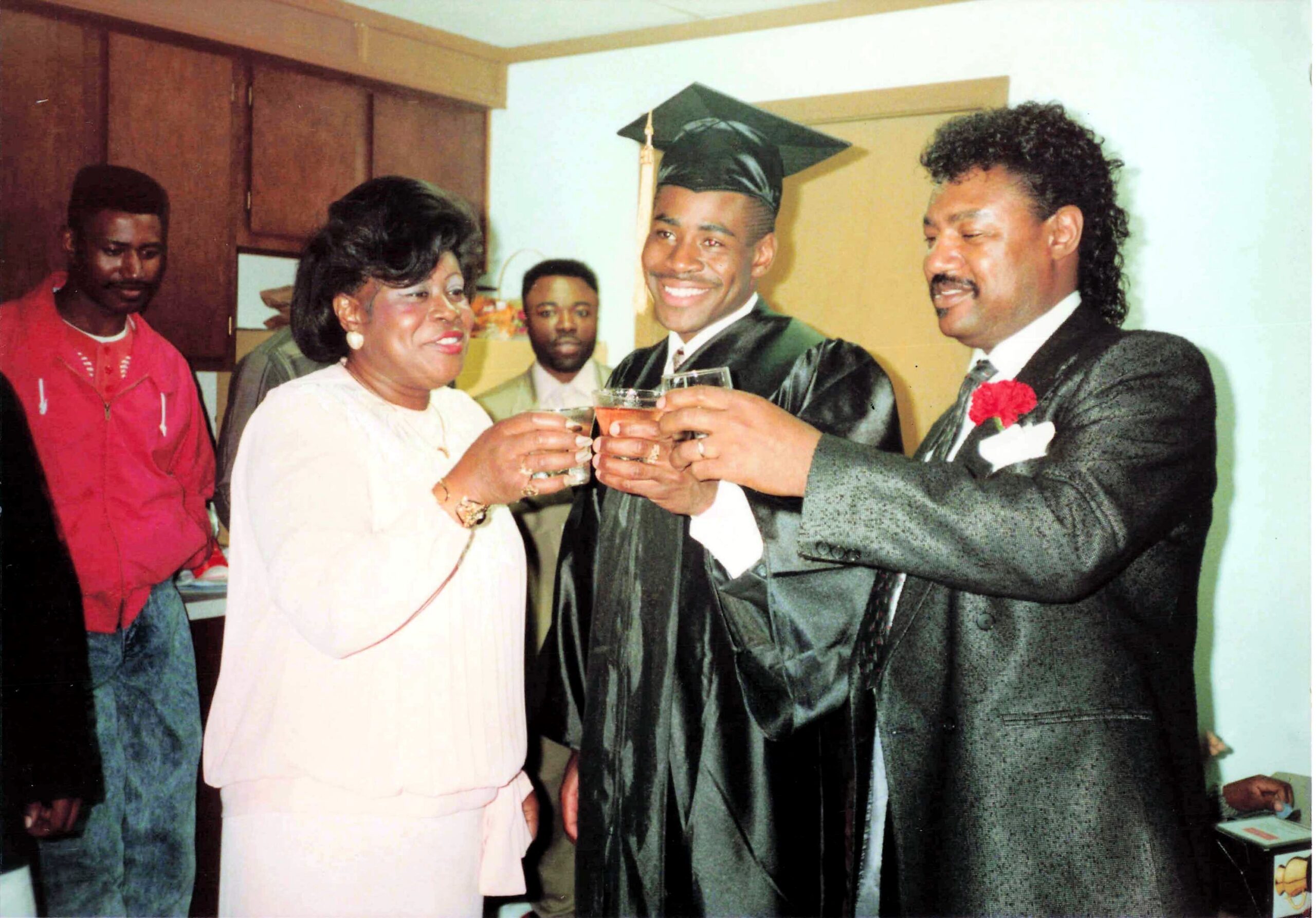 Graduate in cap and gown toasting with a woman in pink dress and a man in a suit at a celebration.