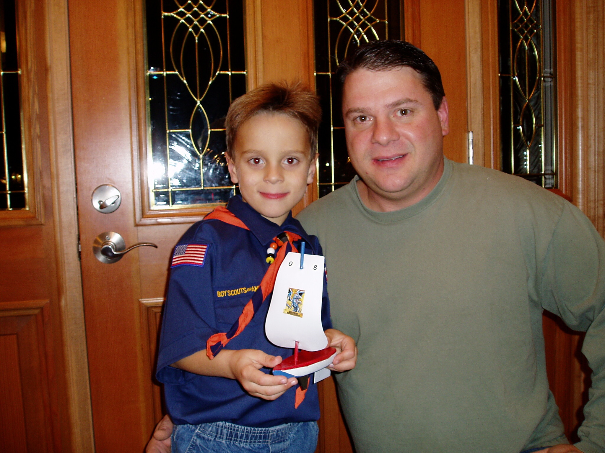 Boy scout in uniform posing with a smiling man in front of a decorative wooden door with glass panels.