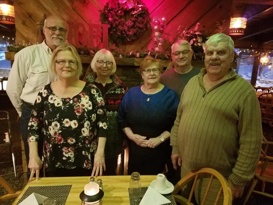 Six adults posing for a group photo in a cozy restaurant, three men and three women around a table with candles and place settings.