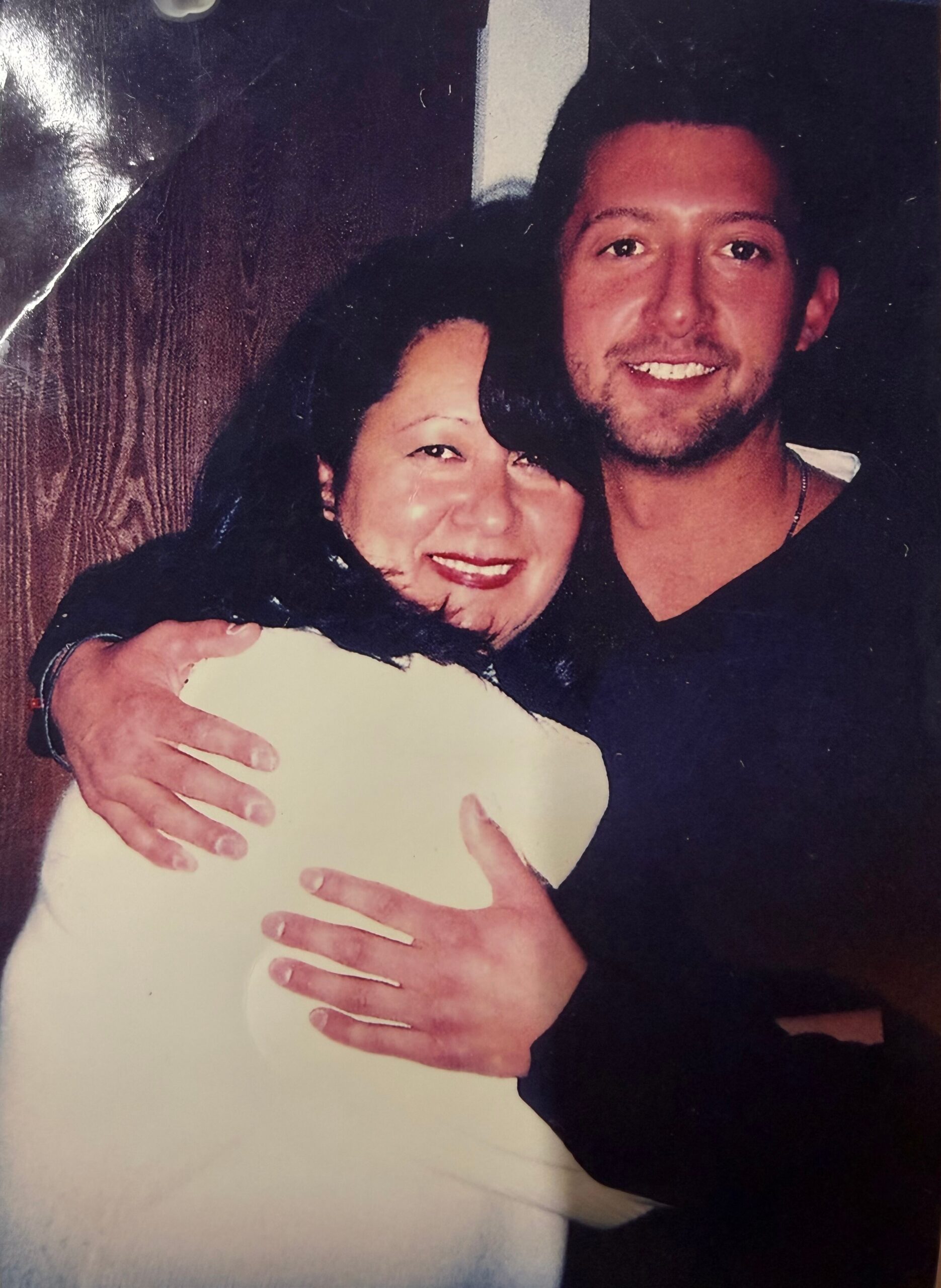 A man and a woman embrace and smile at the camera.