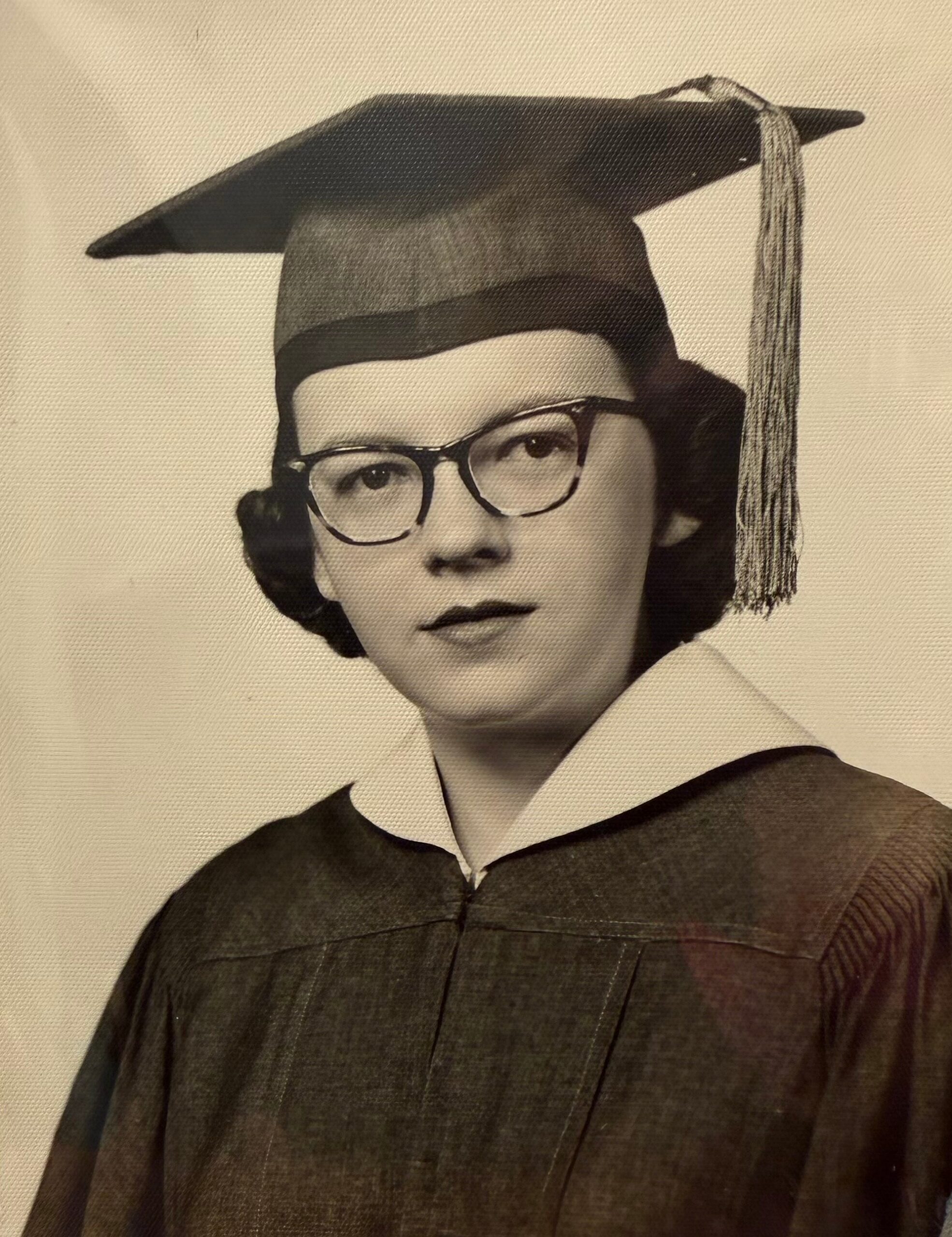 Black-and-white portrait of a graduate wearing a cap and gown with glasses and tassel.
