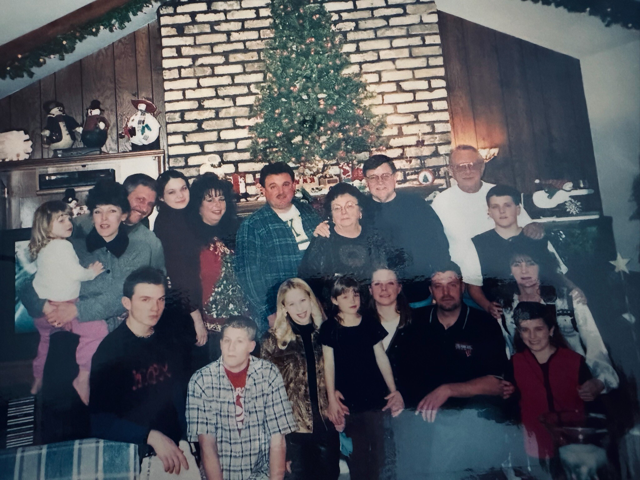 Group of people posing for a holiday photo in a living room with a Christmas tree and a brick fireplace in the background.