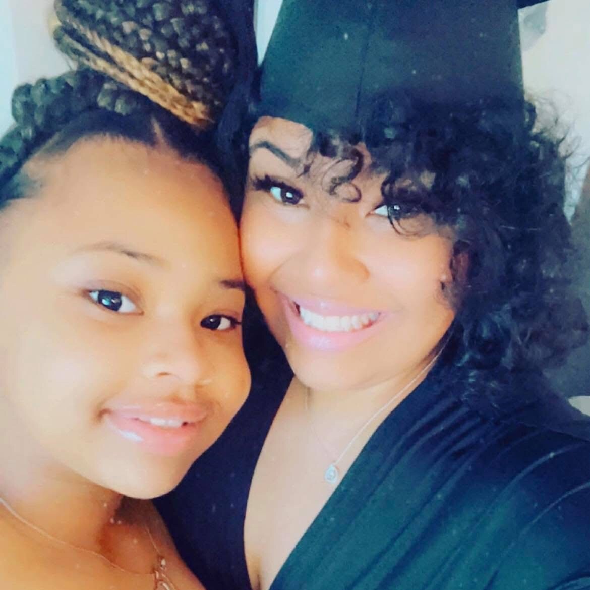 Two women smiling for a selfie, one wearing a graduation cap and gown beside a friend.