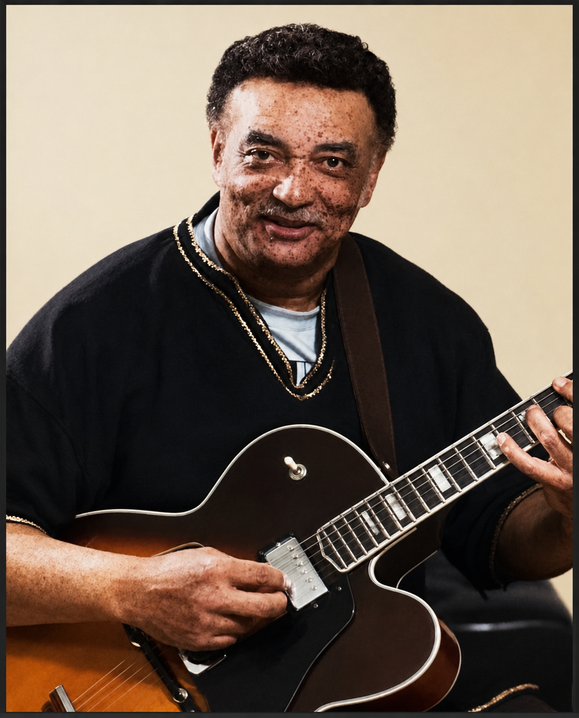Man in a black sweater and gold chains playing a sunburst electric guitar, looking at the camera.