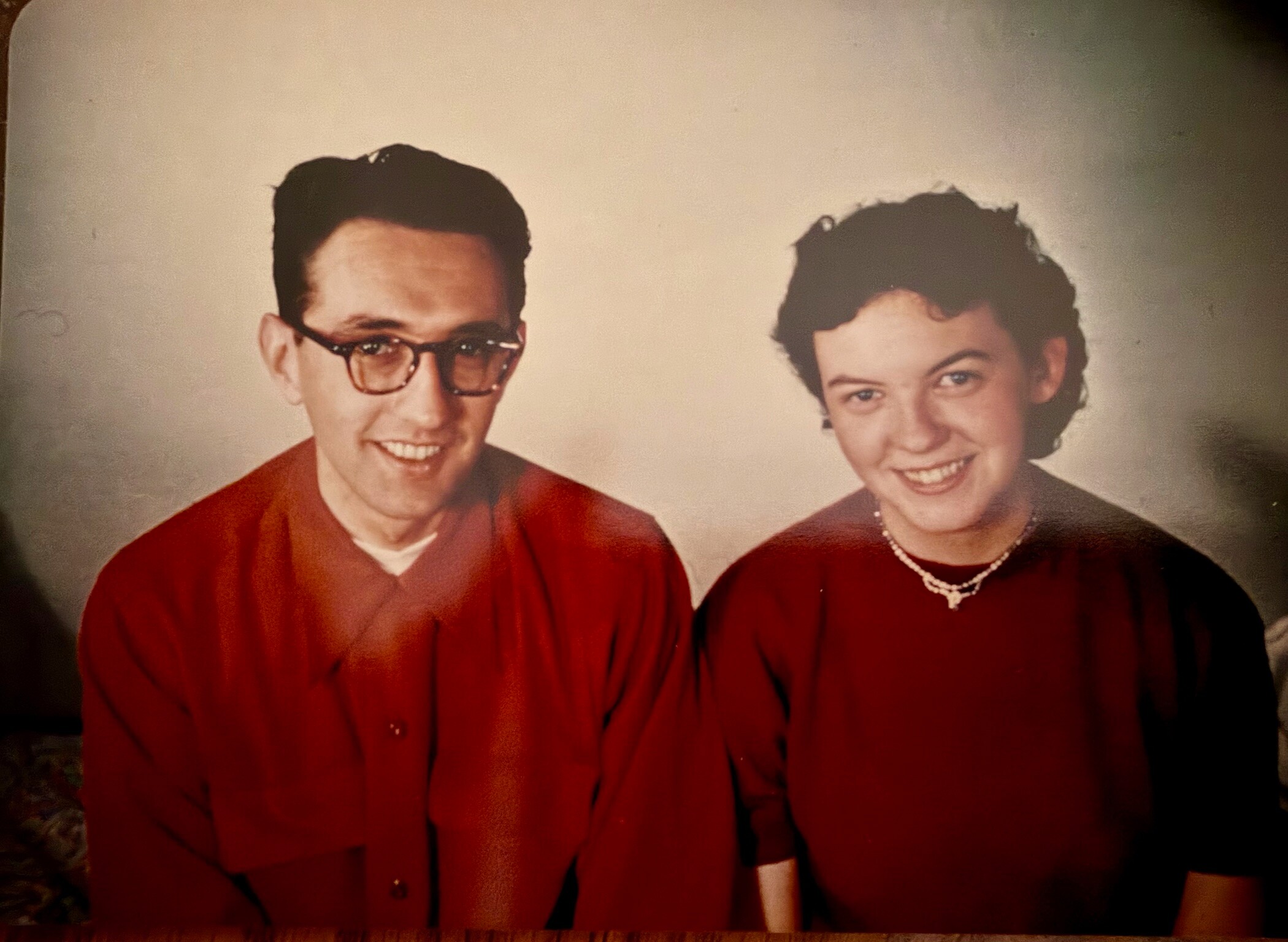Vintage studio portrait of a smiling couple dressed in red, posing side by side in 1950s style.