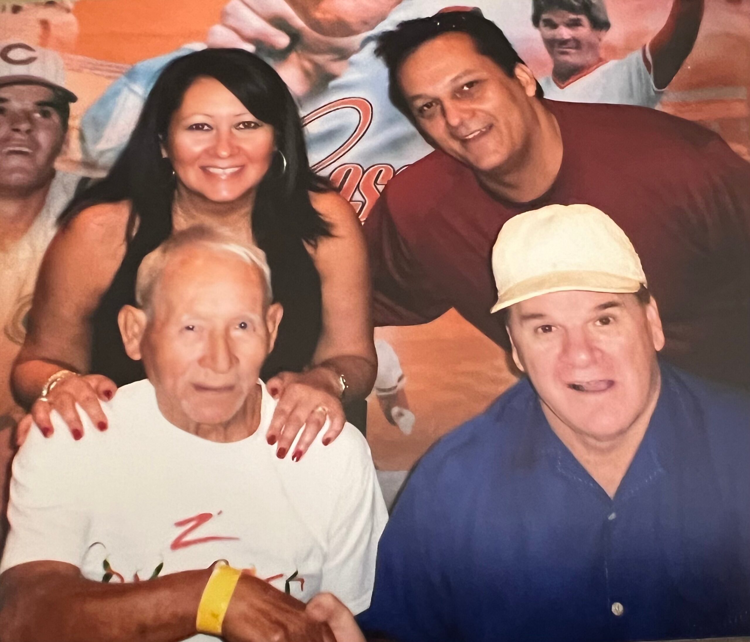 Group photo of adults and children smiling together, with a woman on the left and a man in a maroon shirt center, others around them.