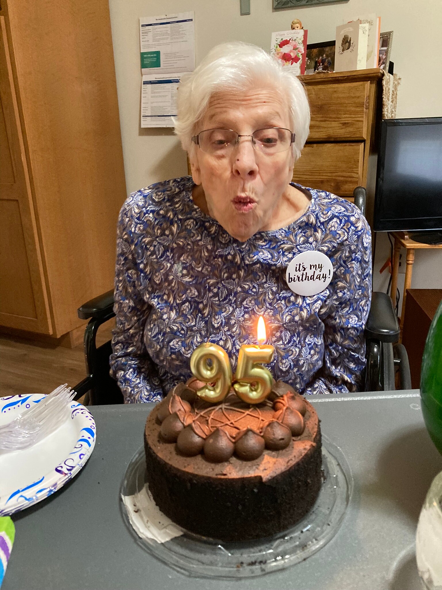 Older woman in a wheelchair wearing a blue floral blouse and a birthday badge that reads 