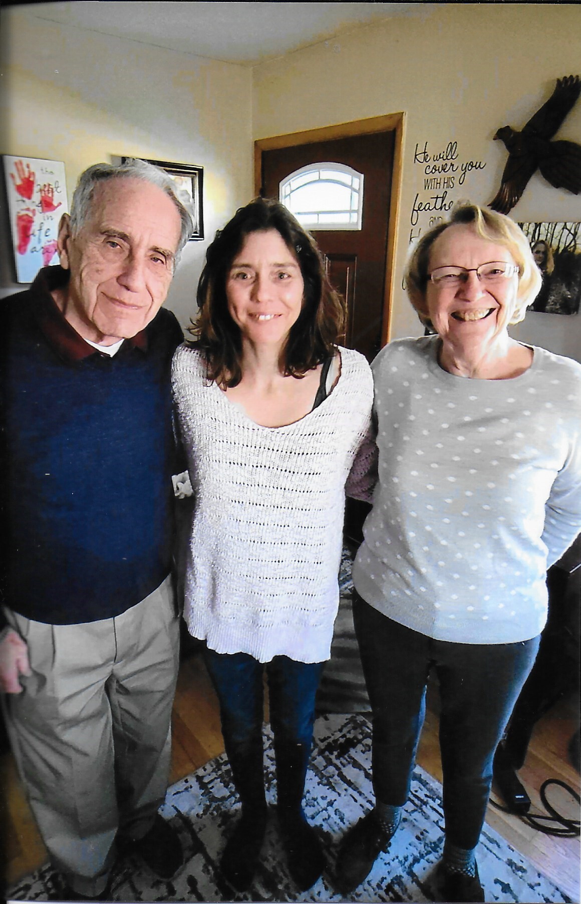 Three people stand side by side in a cozy living room, smiling at the camera.