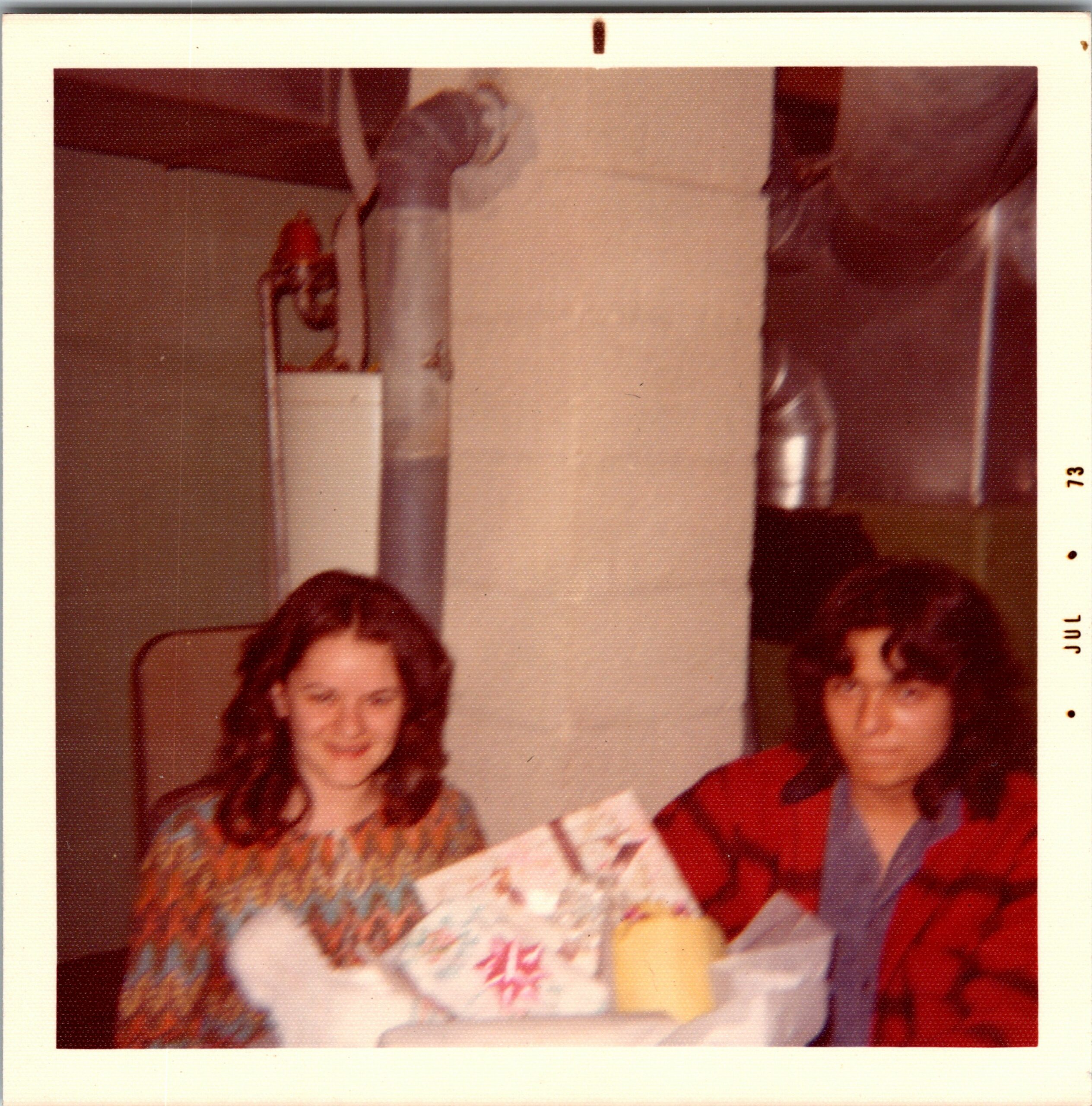 Smiling woman with wavy hair at a cozy birthday gathering; a cake with writing is visible in front.