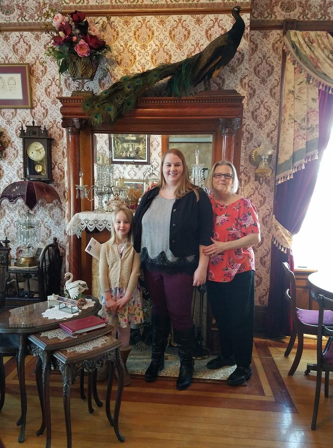 Three generations posing in a vintage parlor with a peacock perched on a wooden cabinet behind them.