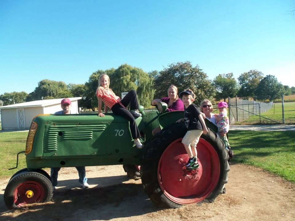 Group of children and adults riding on a green tractor outdoors on a sunny day.
