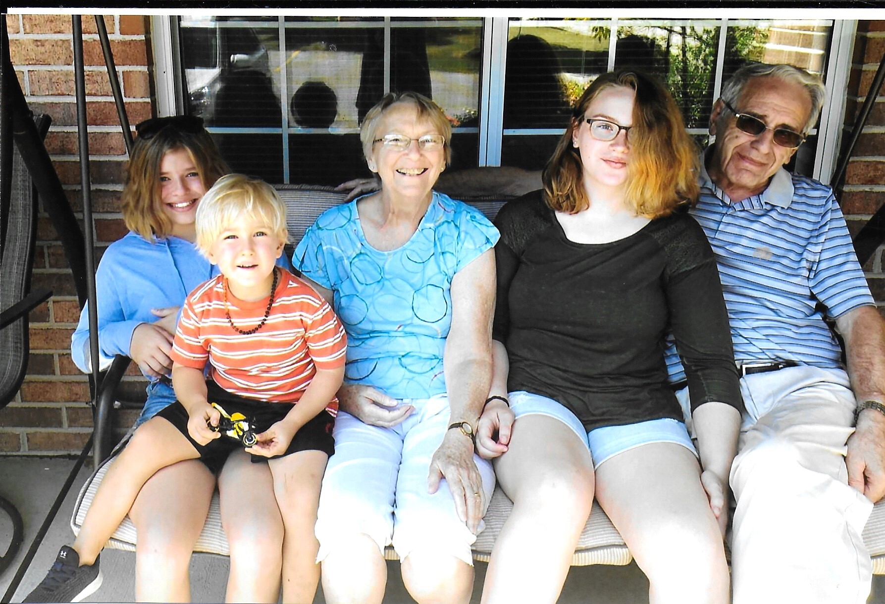 Family of five on a brick porch swing, smiling at the camera.