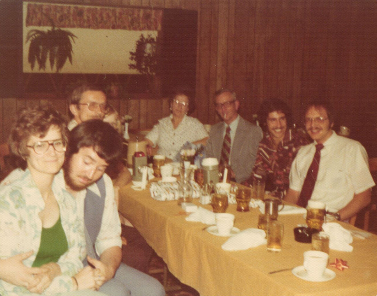 Group of adults seated around a long table with drinks and bowls, smiling and talking in a retro dining room.
