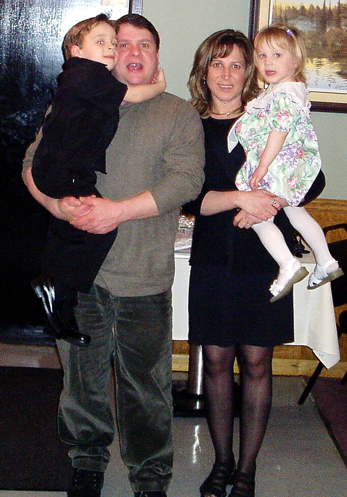 Father holds a young boy while mother holds a little girl indoors, posing for a family photo.