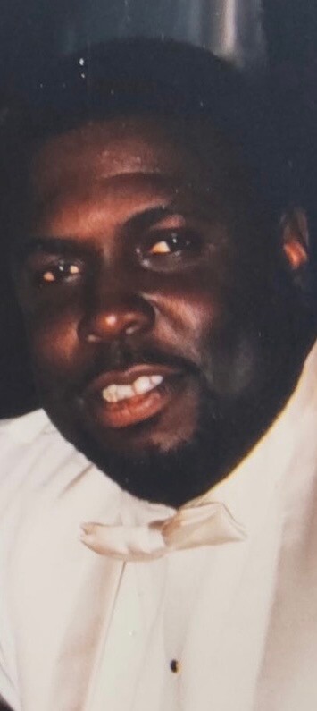 Close-up of a smiling Black man in a white tuxedo shirt and bow tie.