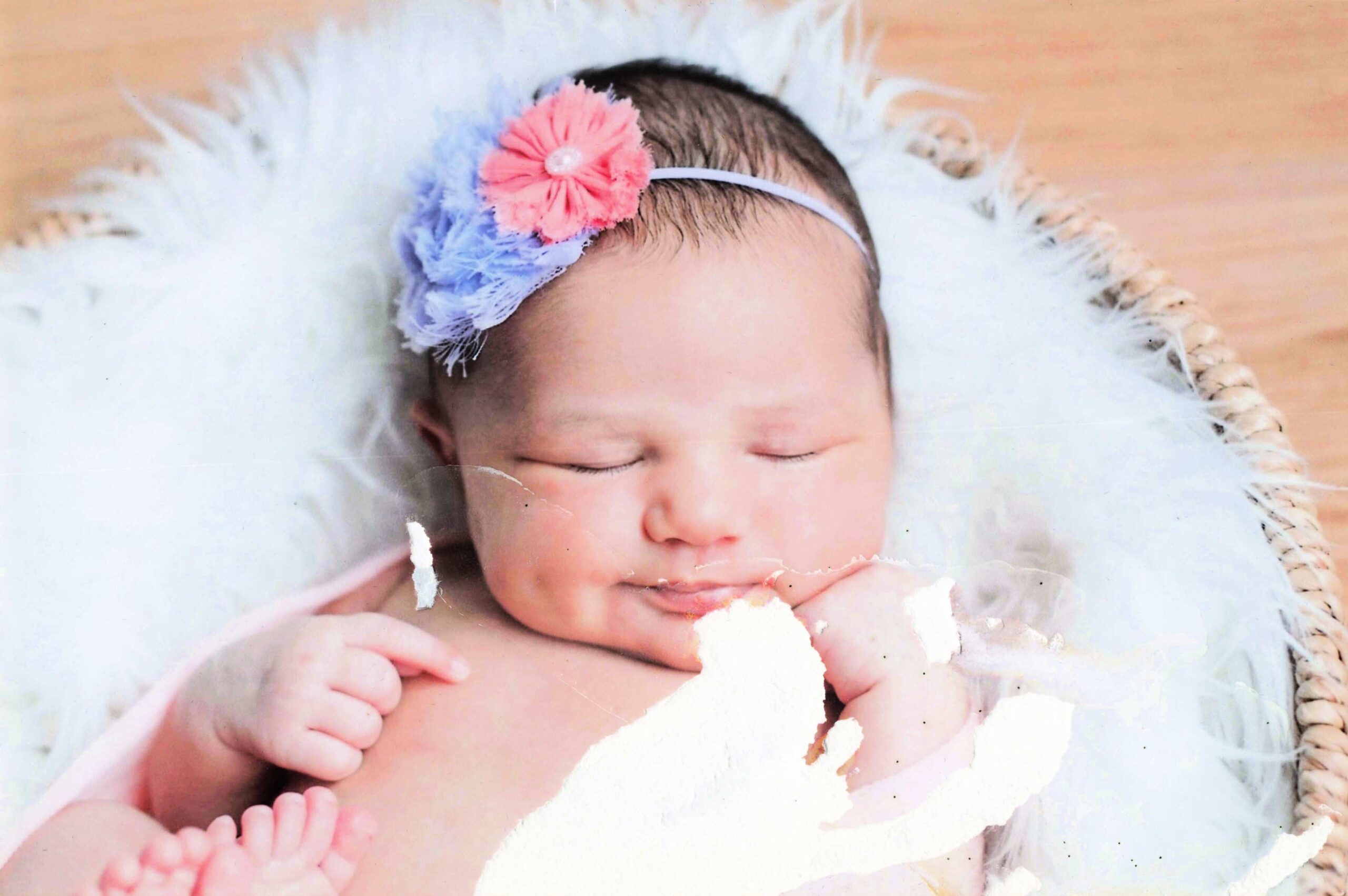 Sleeping newborn with a pastel pink and blue flower headband on a white blanket.