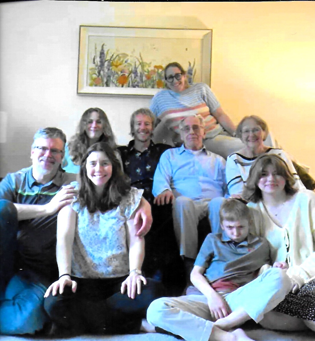 A multi-generational family poses together on a living room sofa, smiling at the camera.