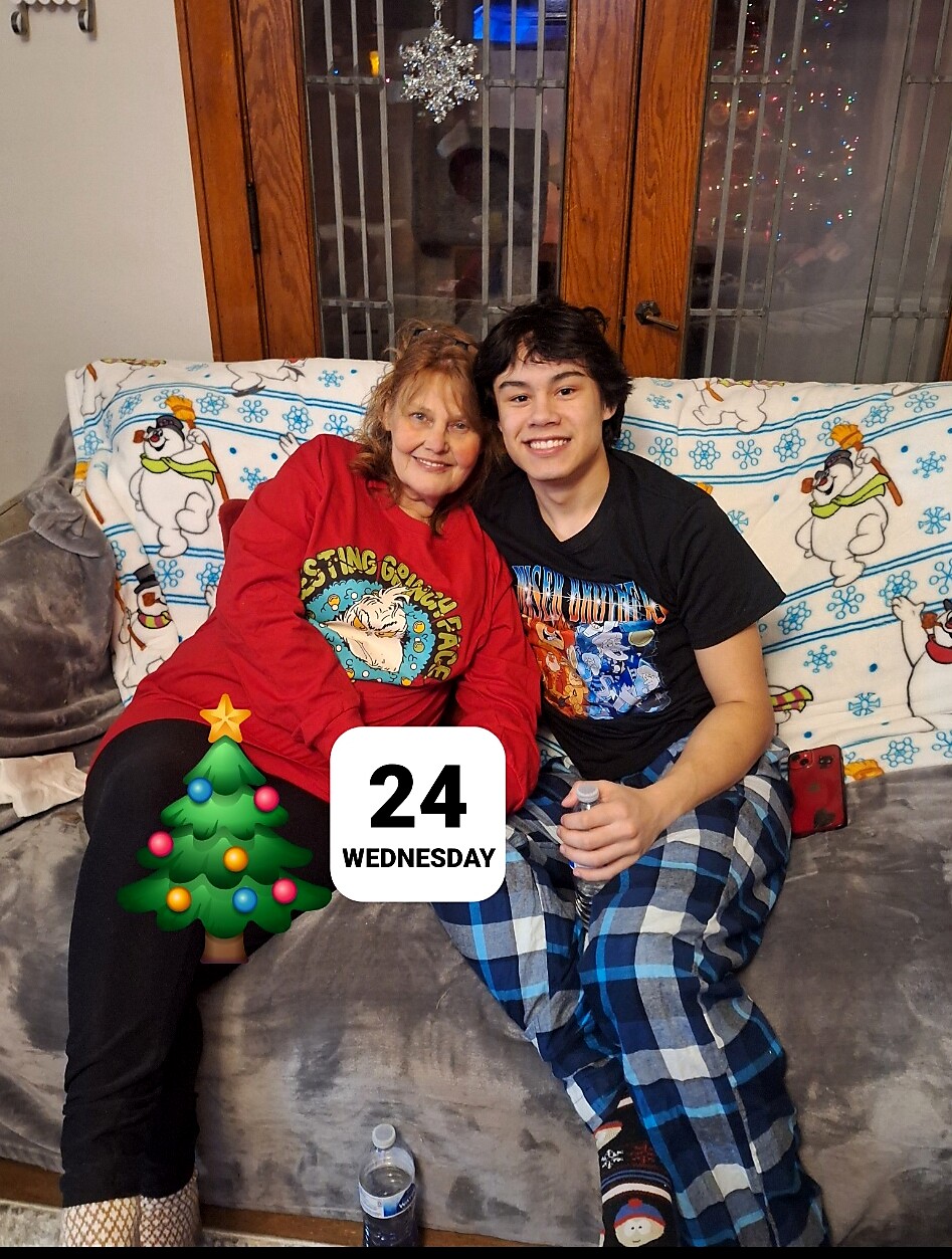 Two people sit close together on a couch, smiling for the camera, with a festive snowflake- and snowman-themed blanket in the background and a Christmas tree sticker partially covering the scene.