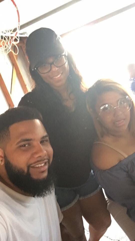 Three friends posing for a selfie indoors with a basketball hoop visible in the background, all smiling at the camera.