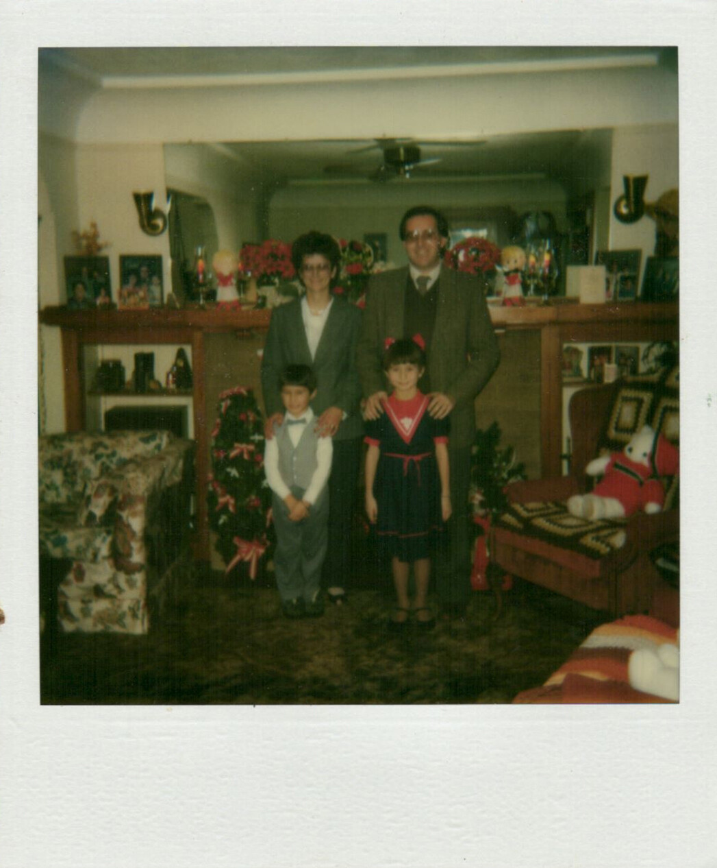 Family of four posing for a holiday photo in a living room with a Christmas tree and gifts nearby.