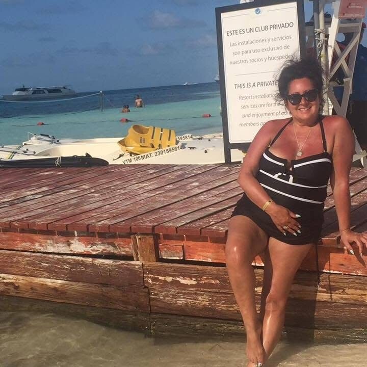 Woman in a black and white swimsuit sitting on a wooden dock by clear turquoise water, with a private club sign nearby.