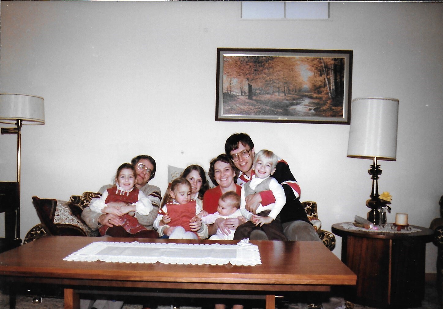 A family group sits closely together on a patterned sofa in a living room, smiling at the camera.