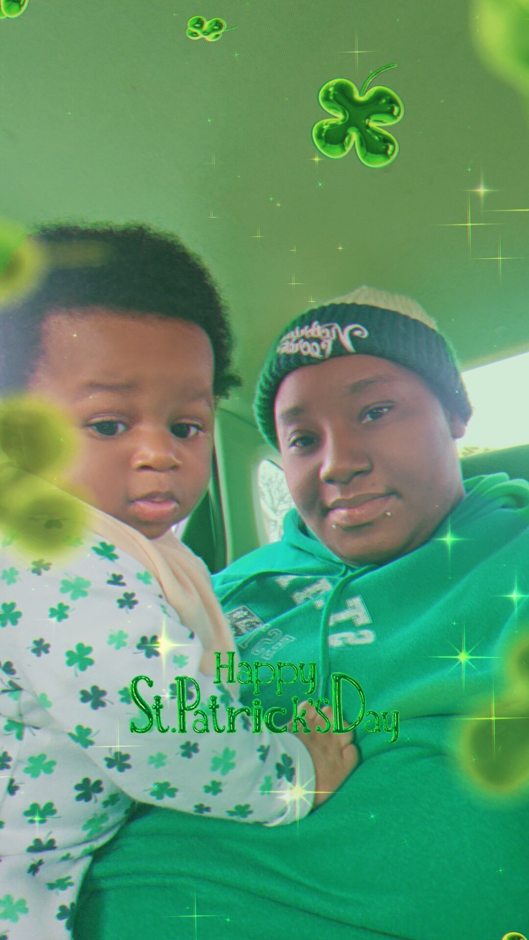 Two people in a car wearing green, with a St. Patrick's Day filter featuring clovers and sparkles.