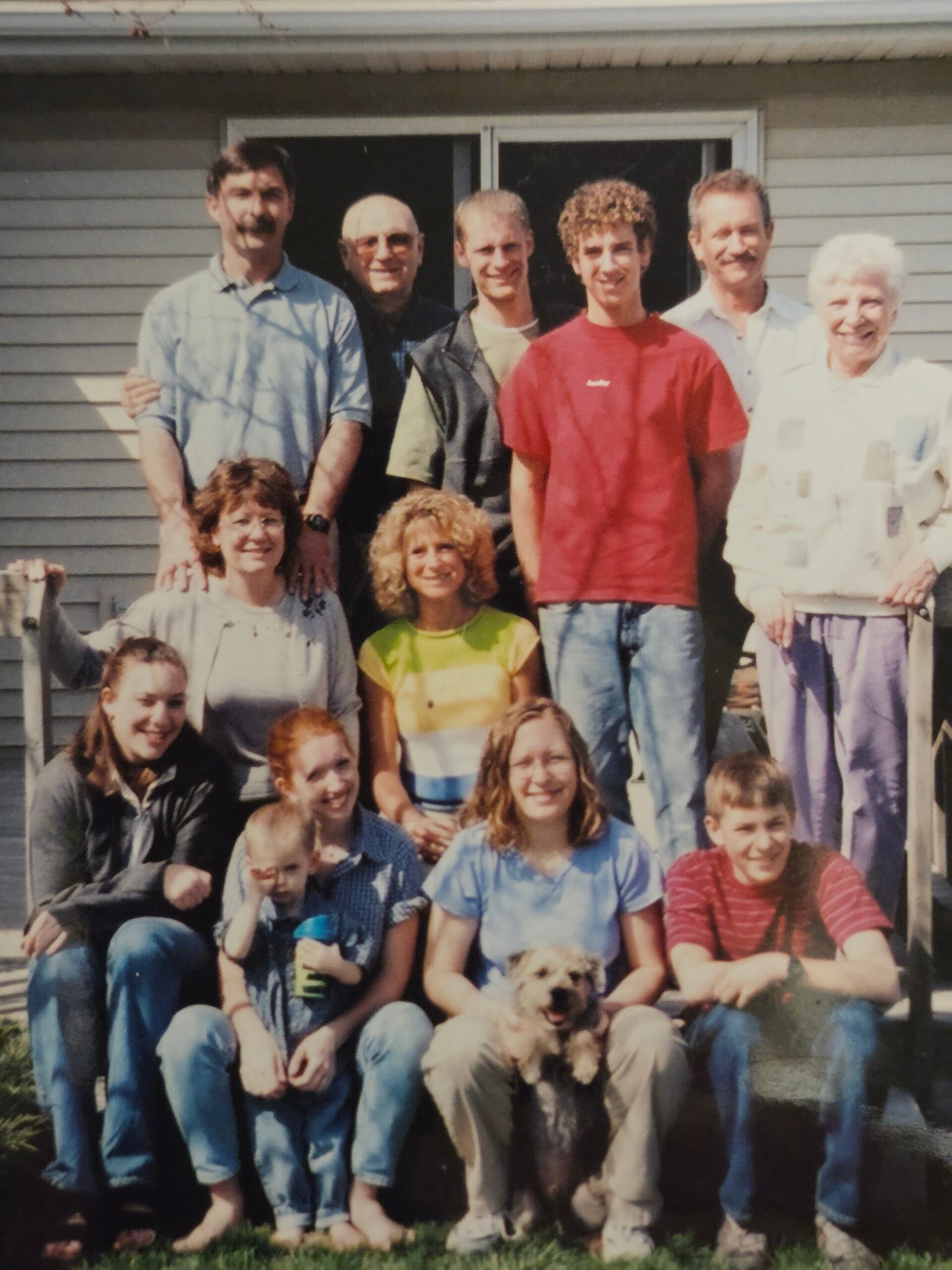 Multi-generational family posing on a front porch with a small dog in front.