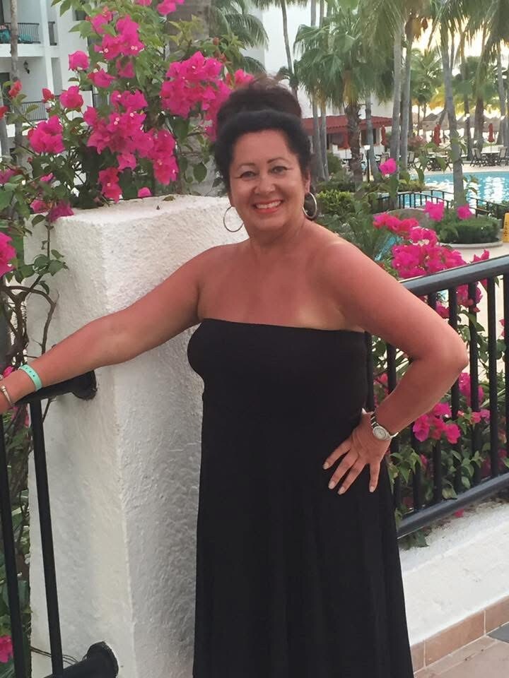 Smiling woman in a black strapless dress poses beside pink flowers and a pool at a resort.