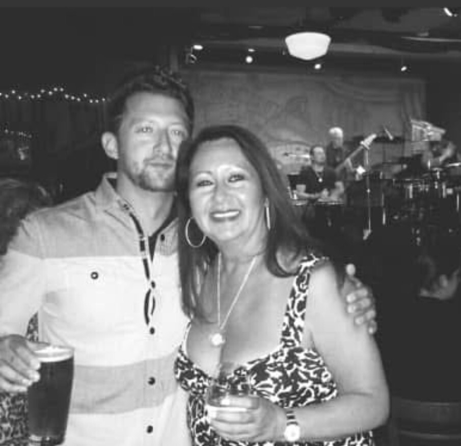 Man and woman posing with drinks at a live music venue; band on stage behind them.
