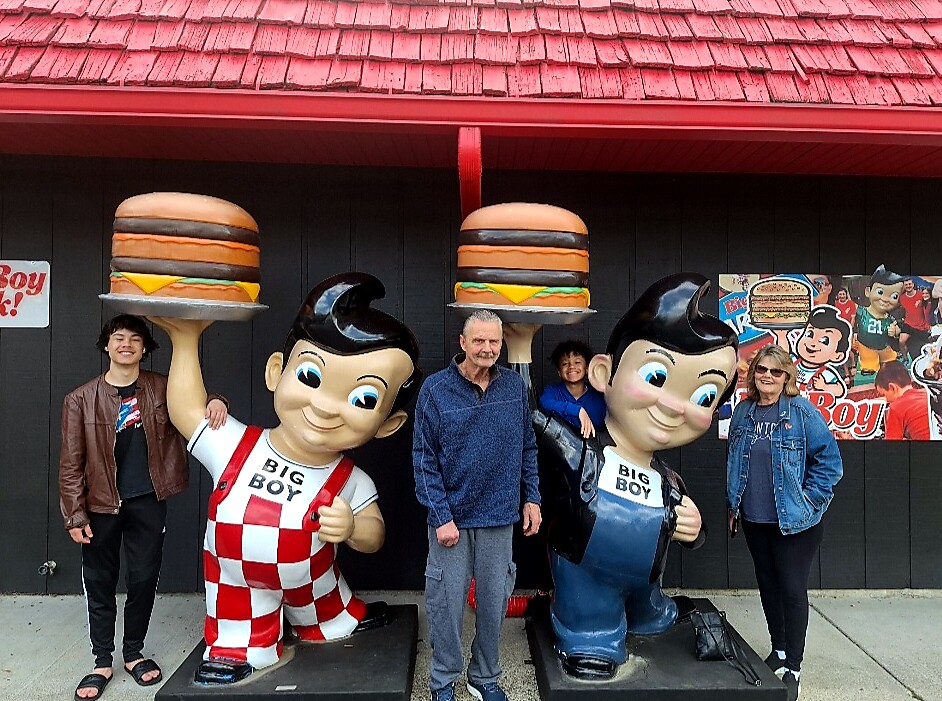 People posing with two oversized Big Boy statues holding giant hamburgers outside a retro diner.