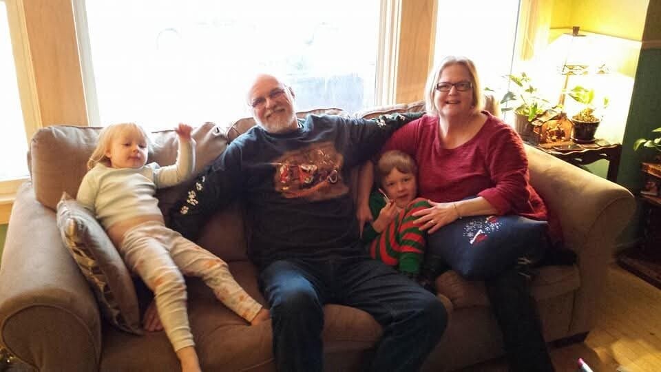 Family of four seated on a beige sofa in a cozy living room, smiling for a casual group photo.